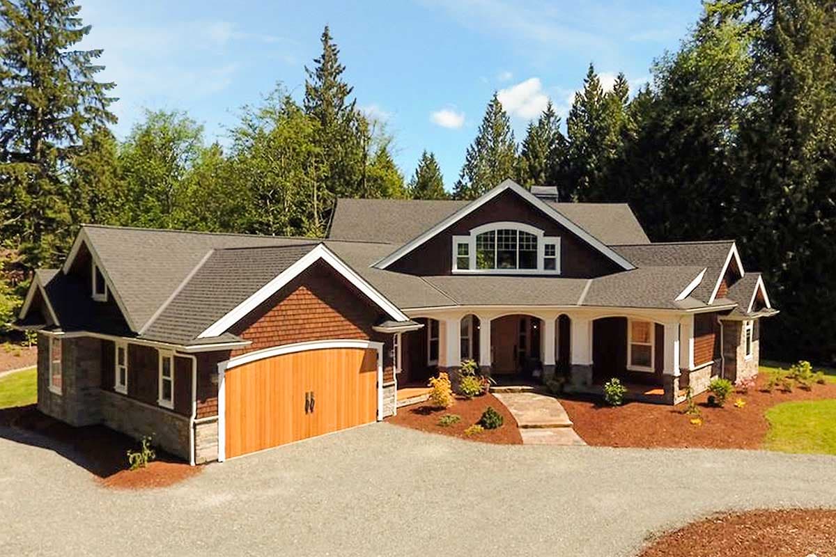 House plan exterior: one-story home with gabled dormers, arched covered entry, stone accents, and attached side-entry garage with wood door.