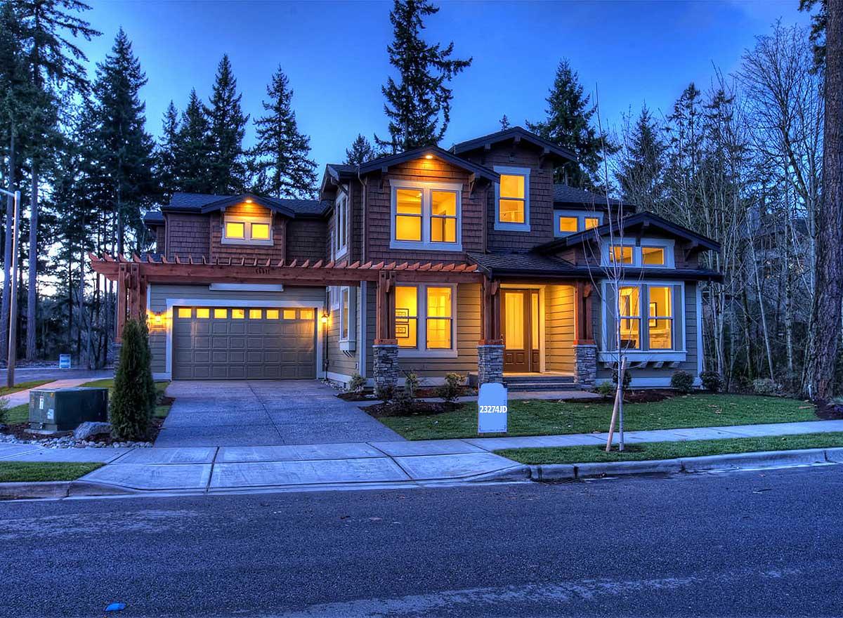 Two-story Modern Farmhouse with wood siding, stone accents, covered front porch, dormers, and attached garage with pergola.