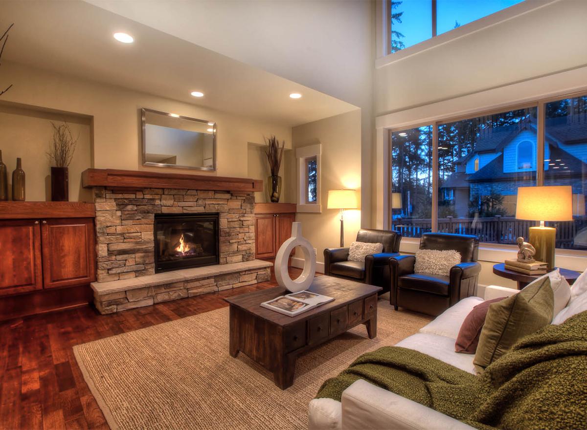 Great room interior rendering with stone fireplace, wood mantel, large windows, and vaulted ceiling.