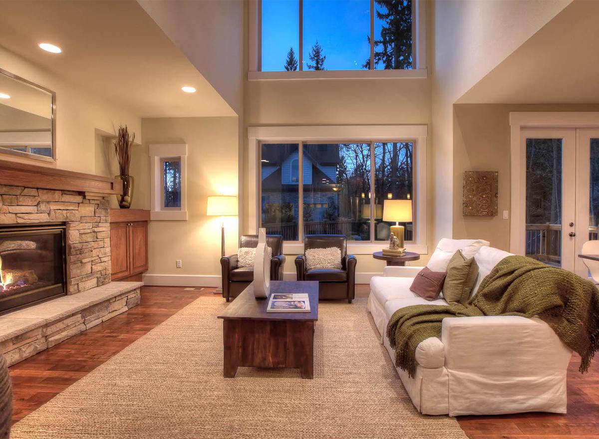 Living room with stone fireplace, vaulted ceiling, and large windows overlooking the outdoors.