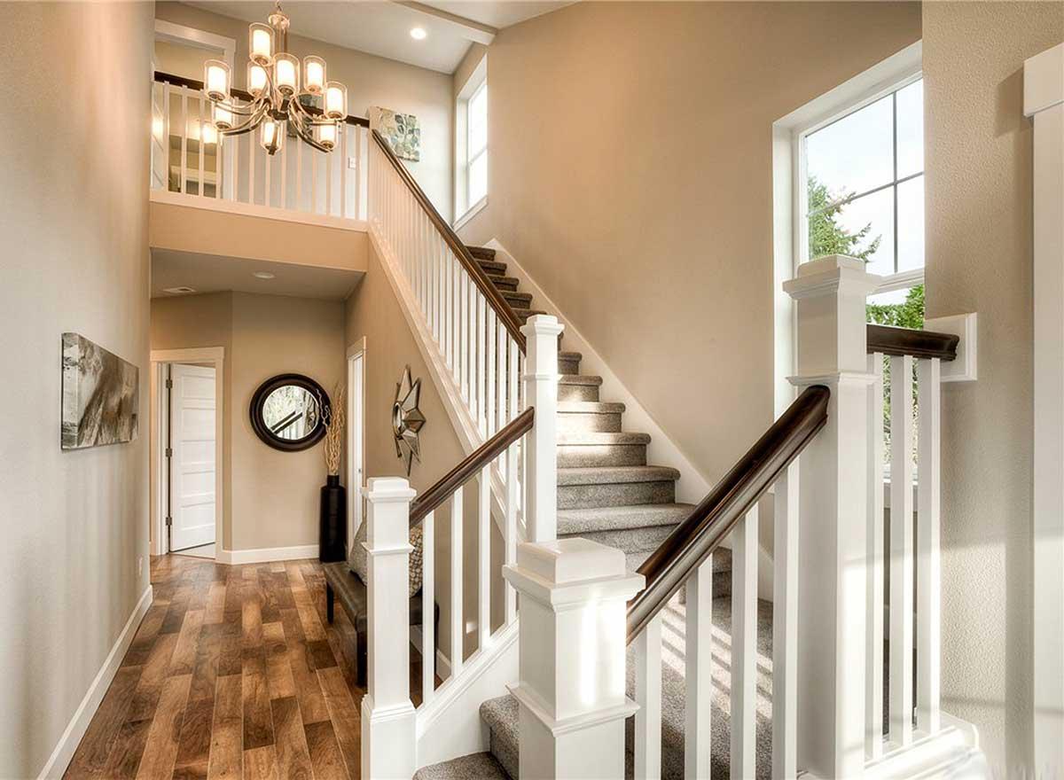 Interior view of a two-story house foyer with a prominent staircase, dark wood flooring, and a chandelier.