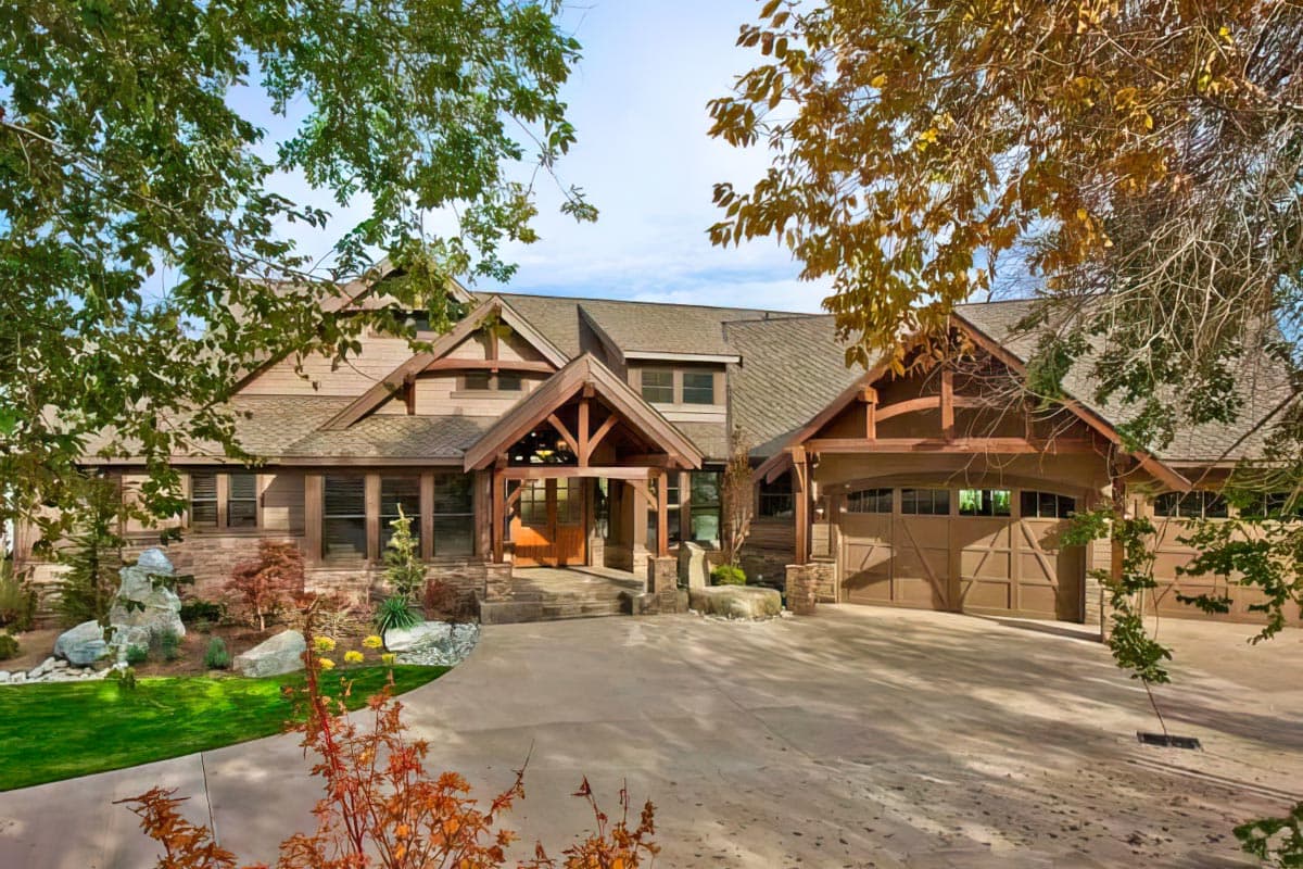 House plan exterior, timber framing accents, covered entry porch, and attached multi-car garage with arched doors.