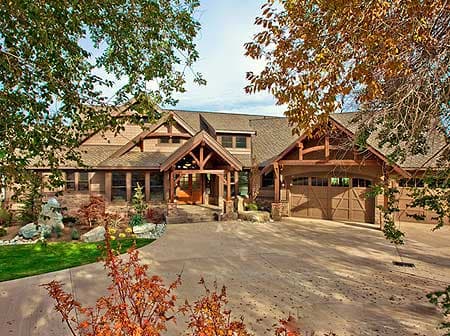 Log-style house plan exterior with a covered entrance porch, prominent wood beams, and a multi-car garage.