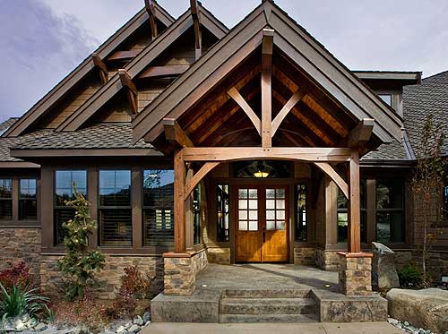 House plan exterior featuring a prominent covered entryway with exposed timber framing, stone accents, and multiple gables.