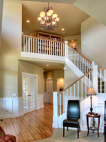 Interior view of a home entryway with a staircase, open loft with bookshelves, and French doors leading to another room.