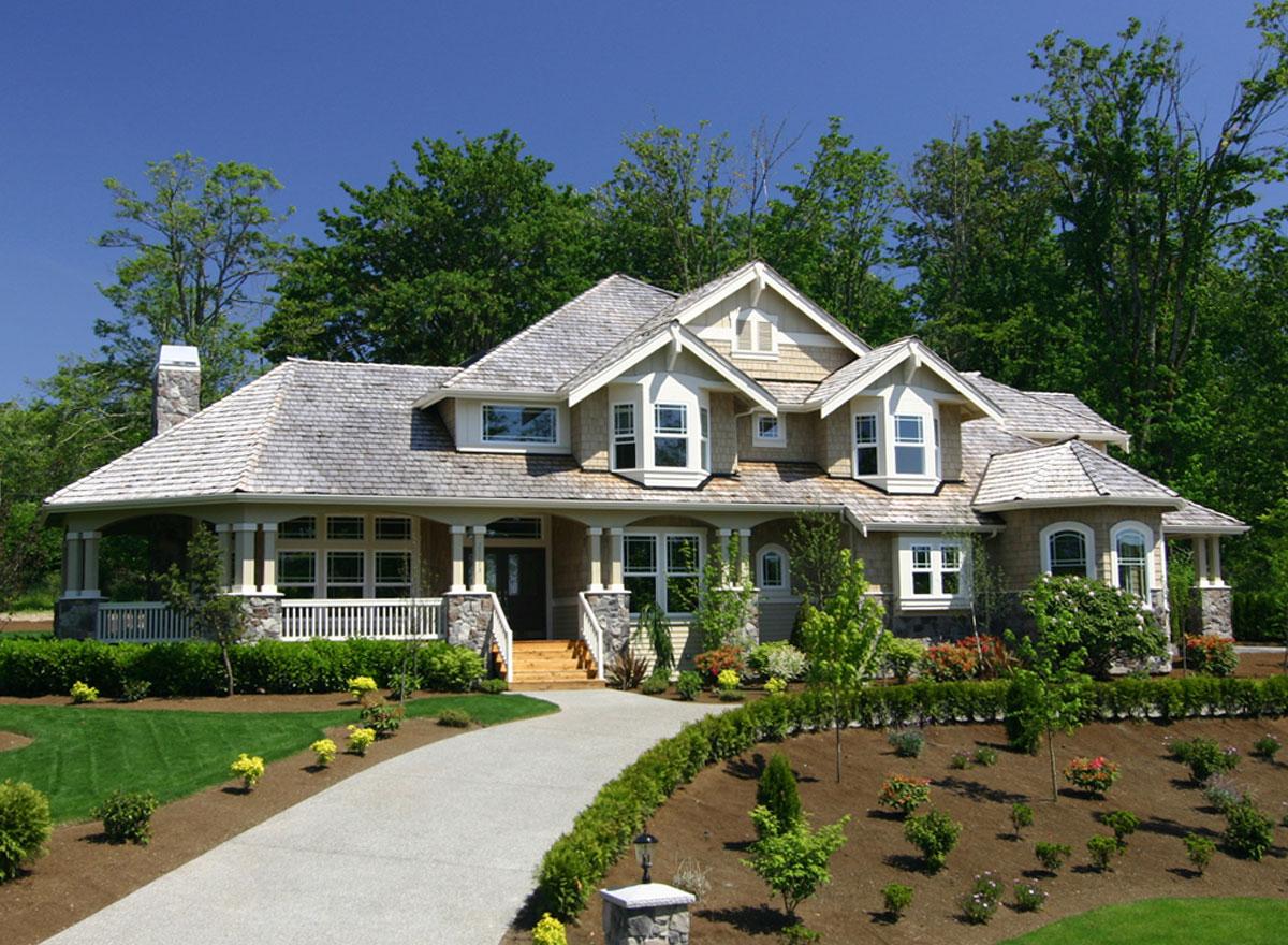House plan exterior: Two-story home with wraparound porch, stone accents, multiple gables, and dormer windows.
