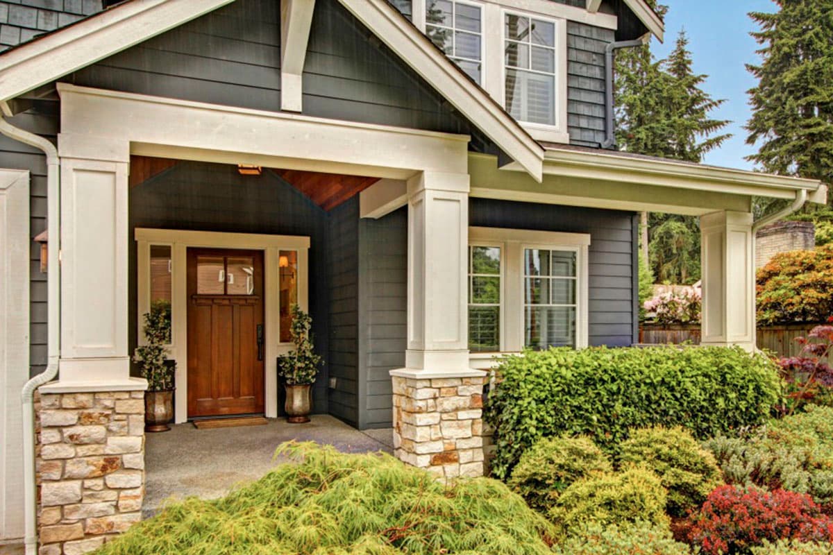 Craftsman style house plan exterior with covered front porch, stone base columns, wood door, and multi-pane windows.