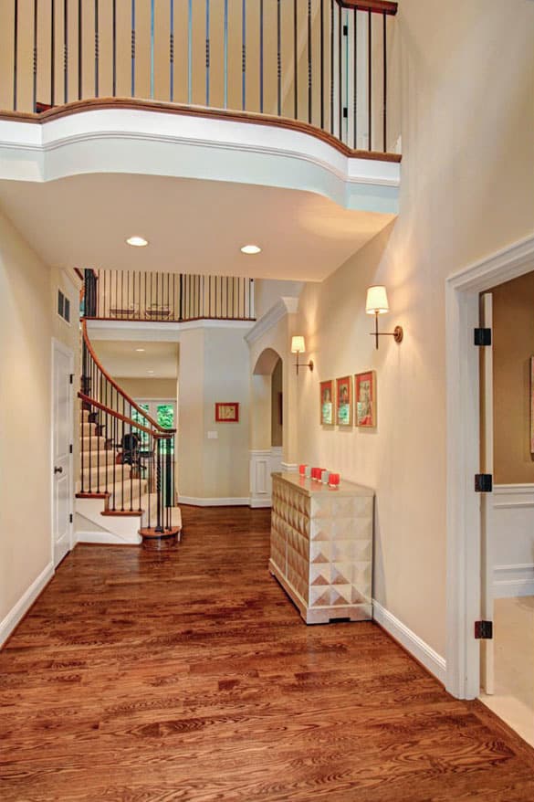 Interior view of a foyer with a curved staircase, second-floor balcony, and hardwood floors.