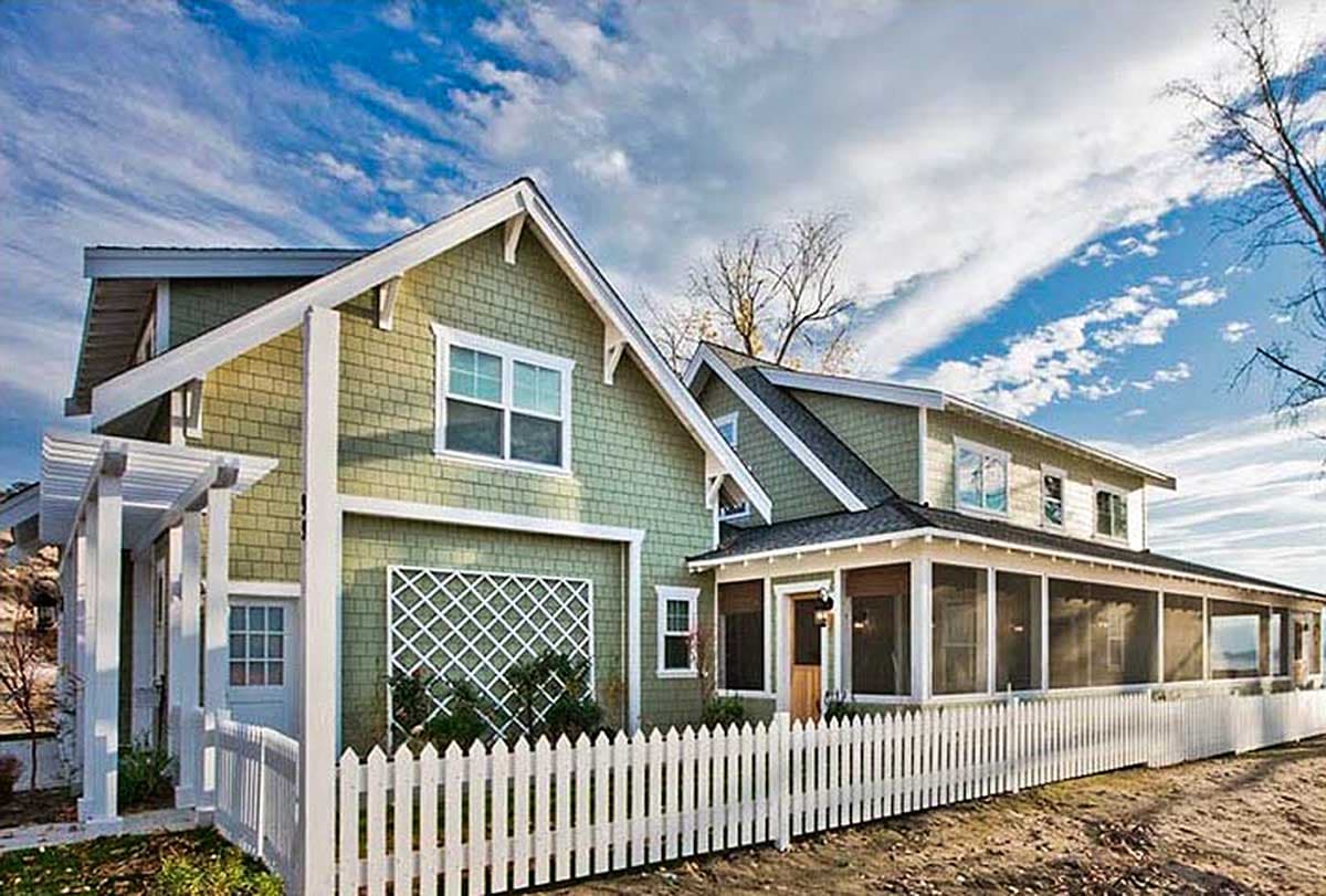 House plan exterior. Two-story Craftsman home with gabled roof, screened porch, and white picket fence. Features include a trellis and dormers.