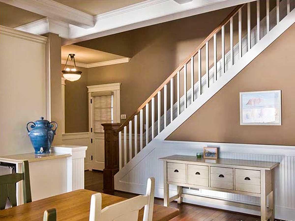 Interior view of a staircase with white balusters and wood handrail, leading to a landing with a pendant light and window.