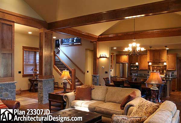 Living room with stone accents, wood beams, fireplace, open to kitchen and dining area with staircase.