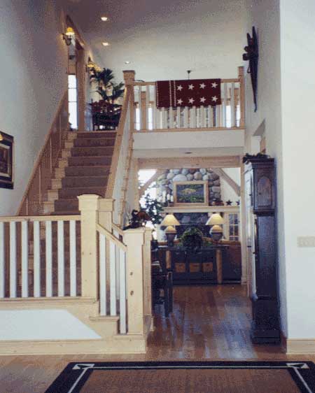 Interior view of a house with a wooden staircase, white balusters, and a stone fireplace visible in the background.