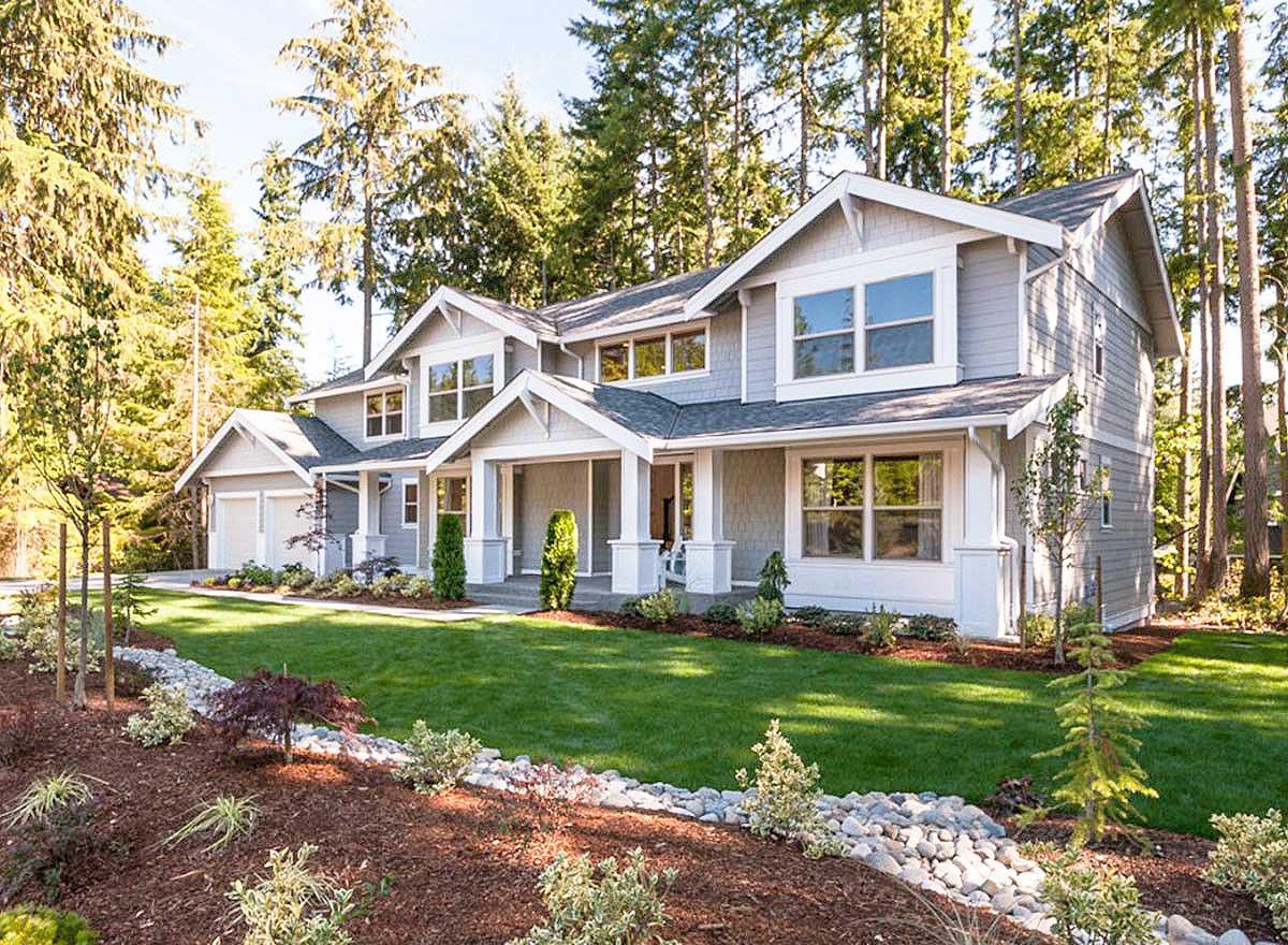 House plan exterior. Two-story Craftsman home with gabled roof, covered porch with columns, and attached garage. Located in a wooded setting.