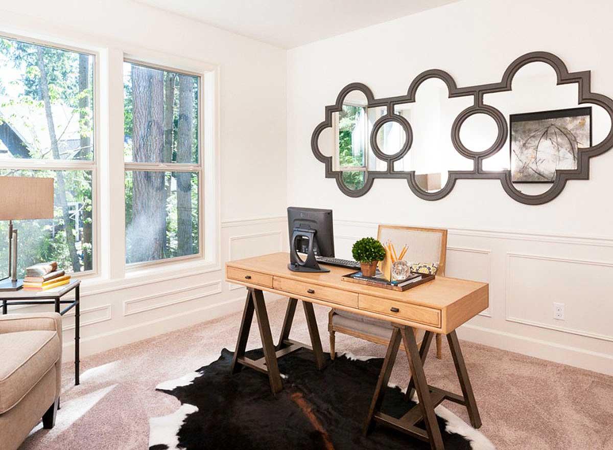 Home office with a wooden desk, computer, chair, large windows, and decorative mirror.