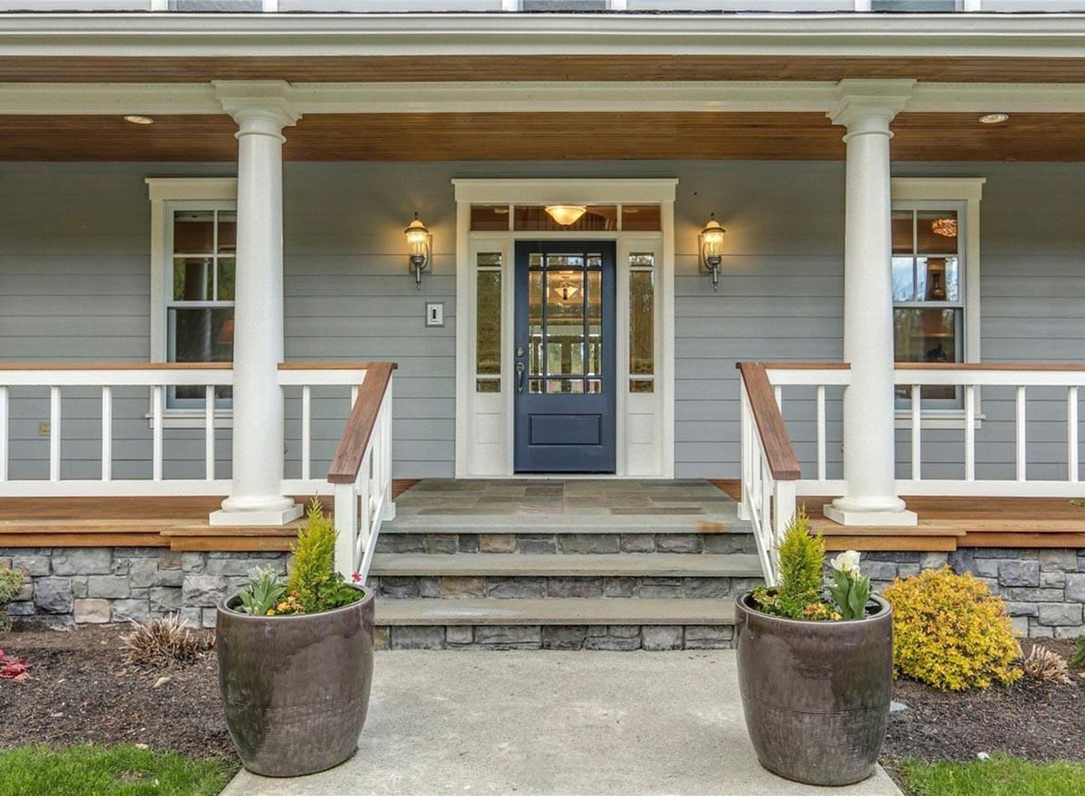 House plan exterior: Modern Farmhouse style with covered porch, stone accents, and a central blue door with sidelights.