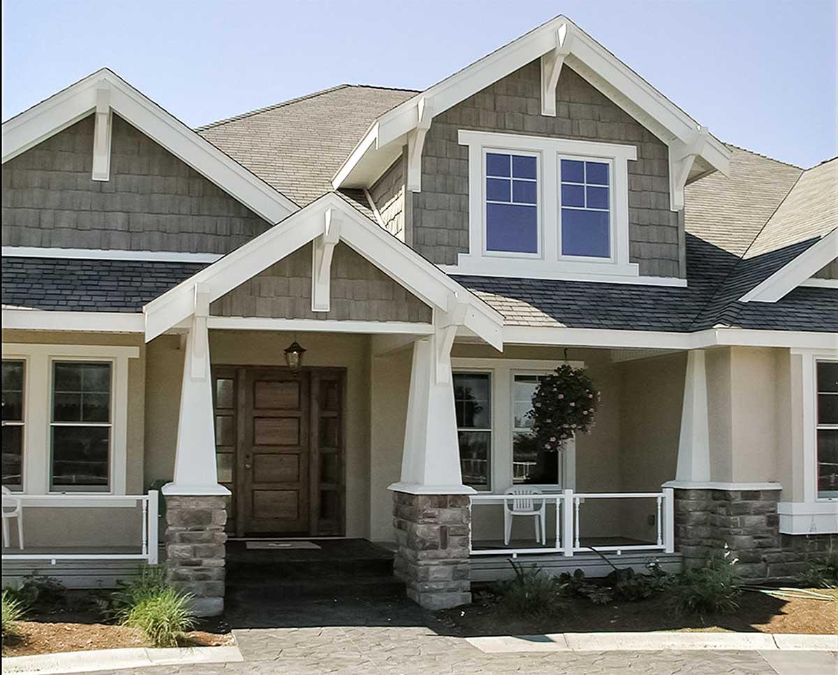 House plan exterior with layered gables, stone accents, a covered entry with a wooden door, and a wrap-around porch.