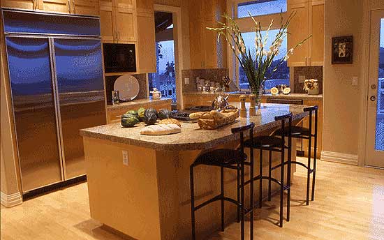Kitchen interior with stainless steel refrigerator, central island with bar stools, granite countertops, and wood cabinetry.