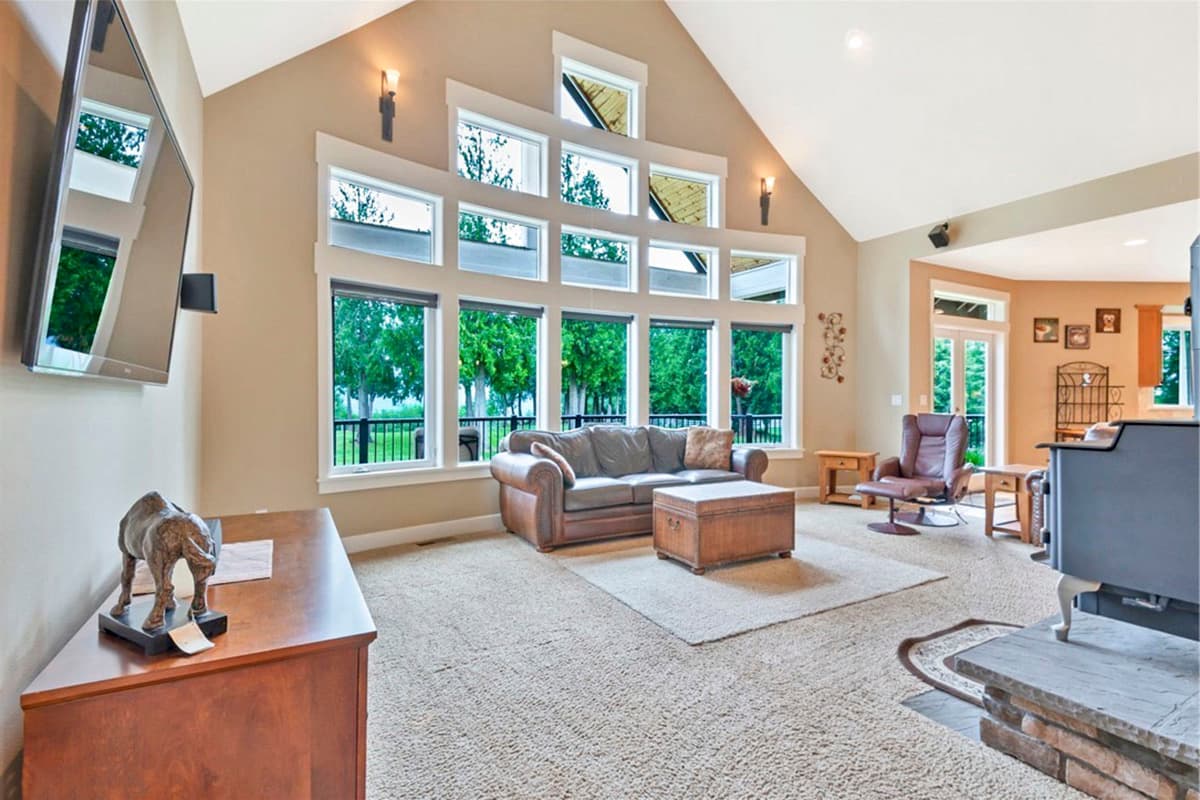 Interior view of living room with vaulted ceiling, large multi-pane window, leather sofa, and stone fireplace.