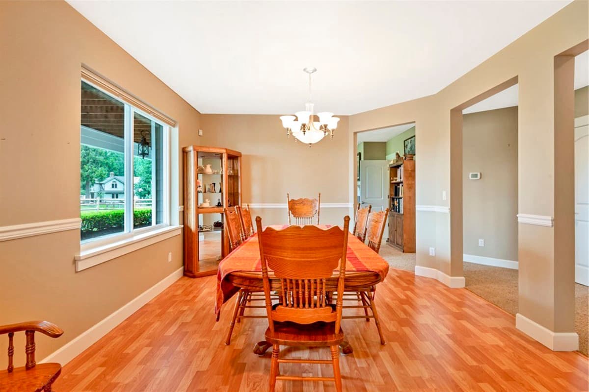 Dining room with wood chairs and table, display cabinet, and large window overlooking a yard.