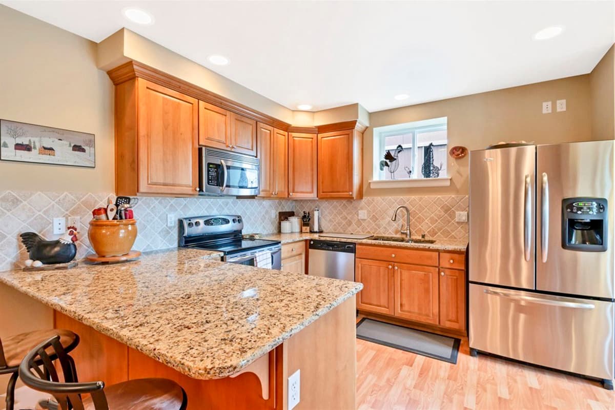 Kitchen with light wood cabinets, granite countertops, stainless steel appliances including a refrigerator with ice dispenser, and a breakfast bar.