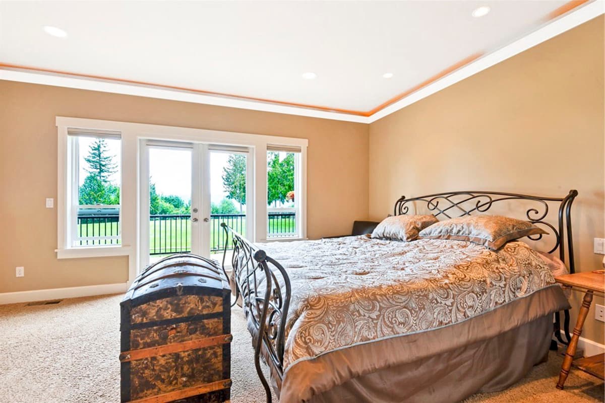 Bedroom interior with king bed, large windows, french doors to balcony, and antique trunk.