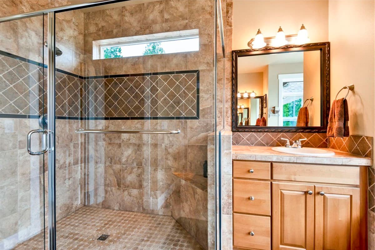 Bathroom interior with glass-enclosed shower with tiled walls and a vanity with wooden cabinets and a mirror.