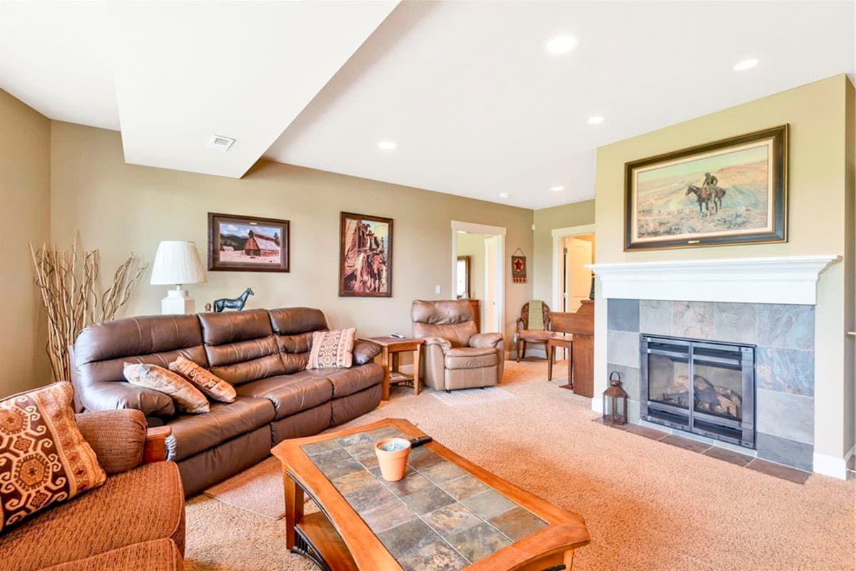 Living room with leather sofa, recliner, tile fireplace, and coffee table. Open doorways lead to other rooms.