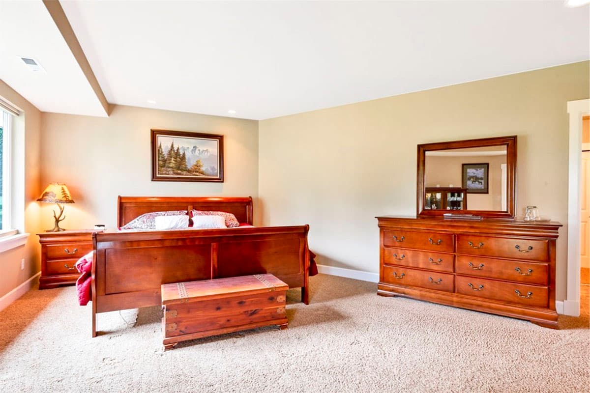 Bedroom with wooden sleigh bed, dresser with mirror, nightstand, cedar chest, and large window.