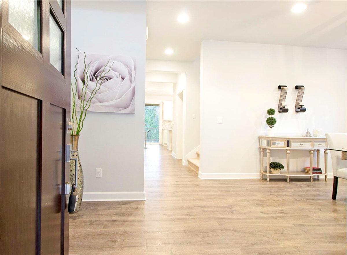 Interior view of entryway with dark wood door, light wood flooring, and hallway leading to kitchen.