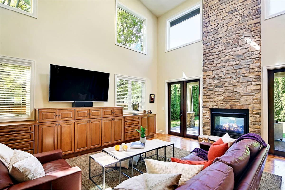 Living room with vaulted ceiling, stone fireplace, built-in cabinetry, and large windows.