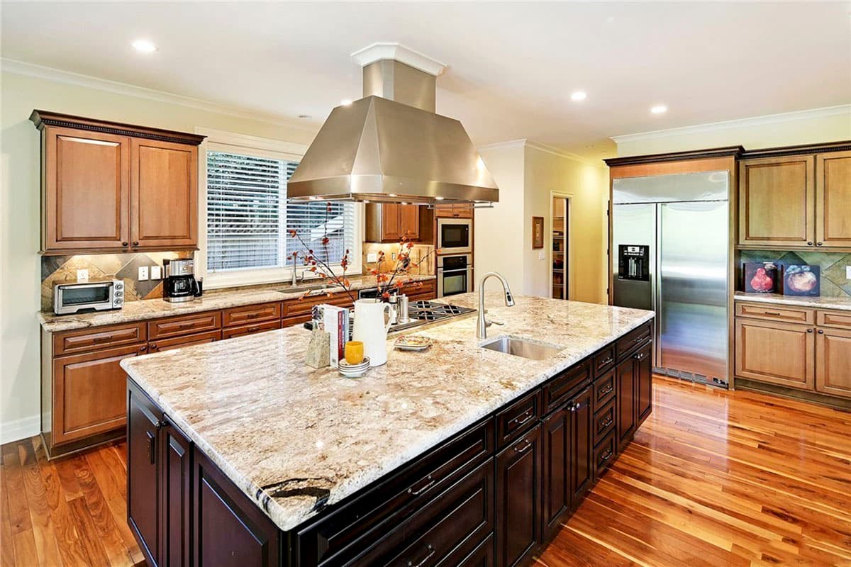 Kitchen with large island, granite countertops, stainless steel range hood and appliances, and wood cabinetry.