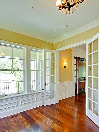 Interior view of room with French doors, multi-pane windows, wainscoting, and hardwood floors.