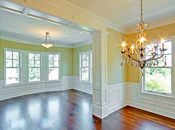 Interior view of a dining room with wainscoting, large windows, crown molding, and a chandelier.
