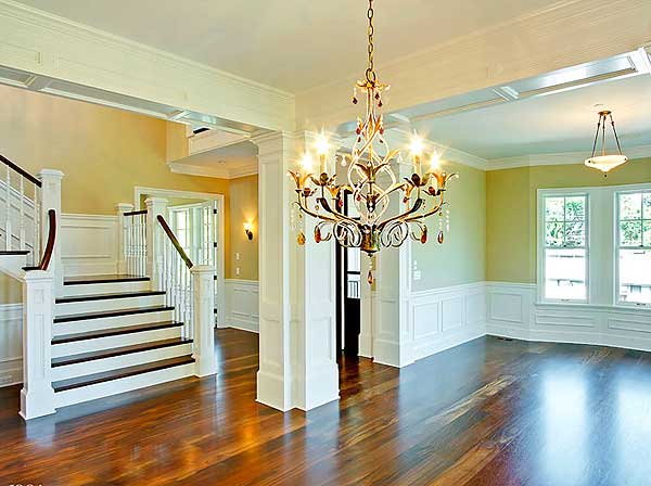 Interior view of a home entry with a grand staircase, ornate chandelier, and wainscoting.