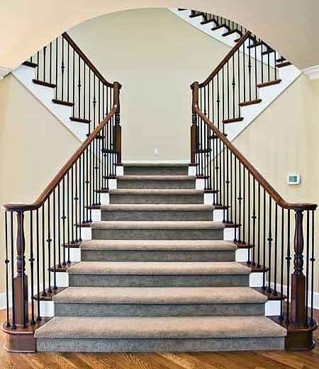 Grand staircase with carpeted treads, wood railings, and ornate balusters leading to upper level.