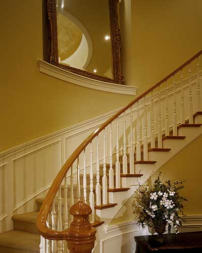 Curved staircase with ornate balusters, wainscoting, and a large decorative mirror.