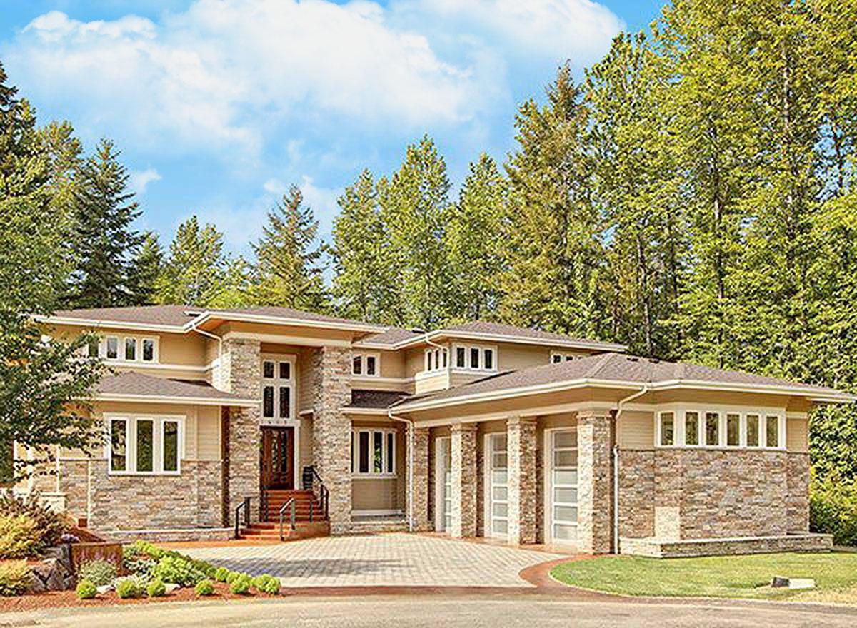 House plan exterior. Two-story home with stone accents, flat roof, and multiple windows. Features a covered porch and attached garage.