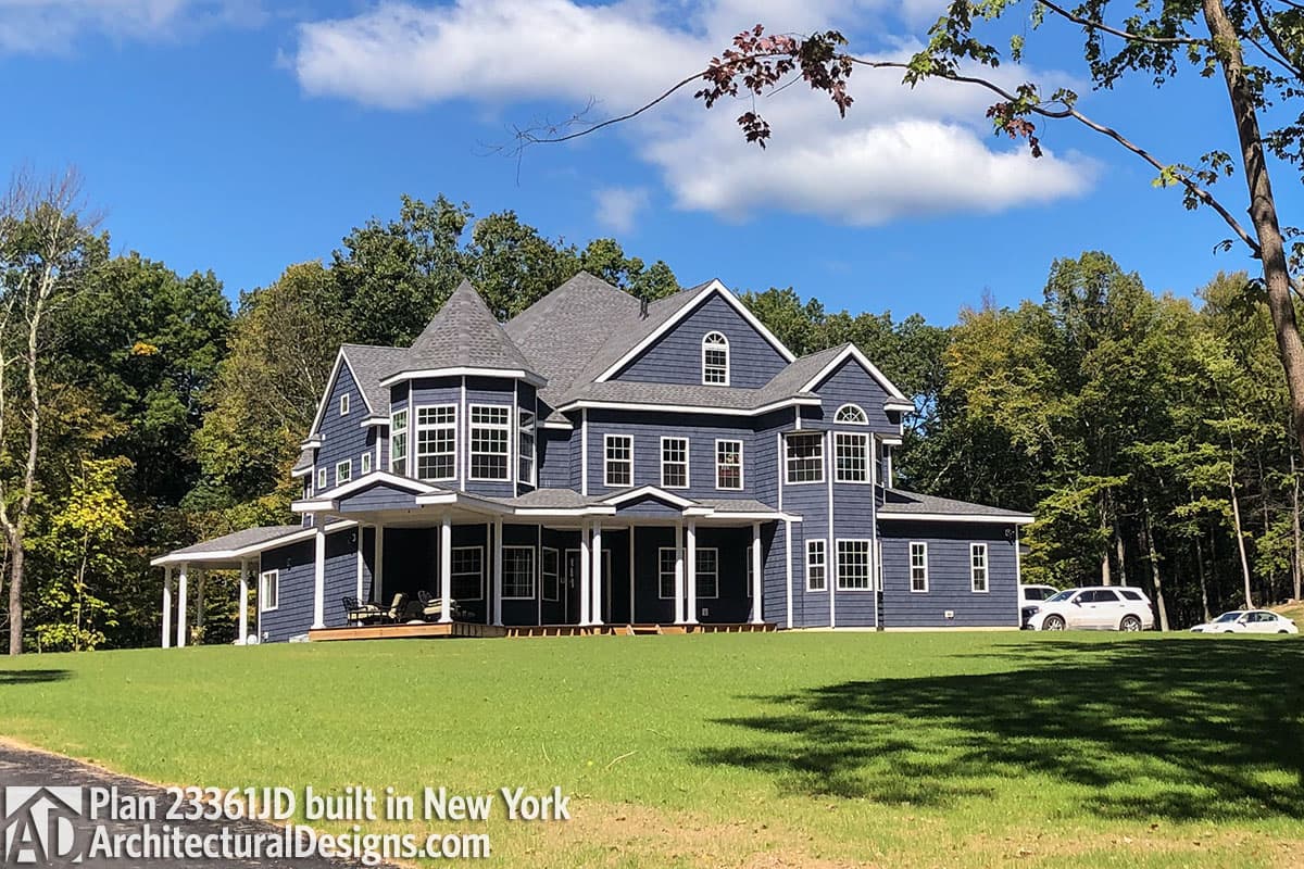 House plan exterior: Large blue shingle-sided home with a wrap-around porch, dormers, and a turret.