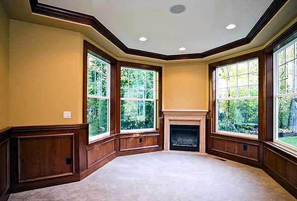 Interior view of room with fireplace, bay windows, wood paneling, and crown molding. Carpeted floor.