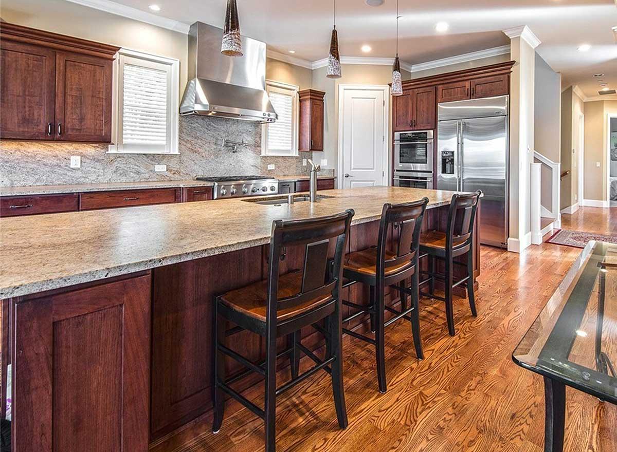 Kitchen with large island, granite countertops, stainless steel appliances, dark wood cabinetry, and pendant lighting.