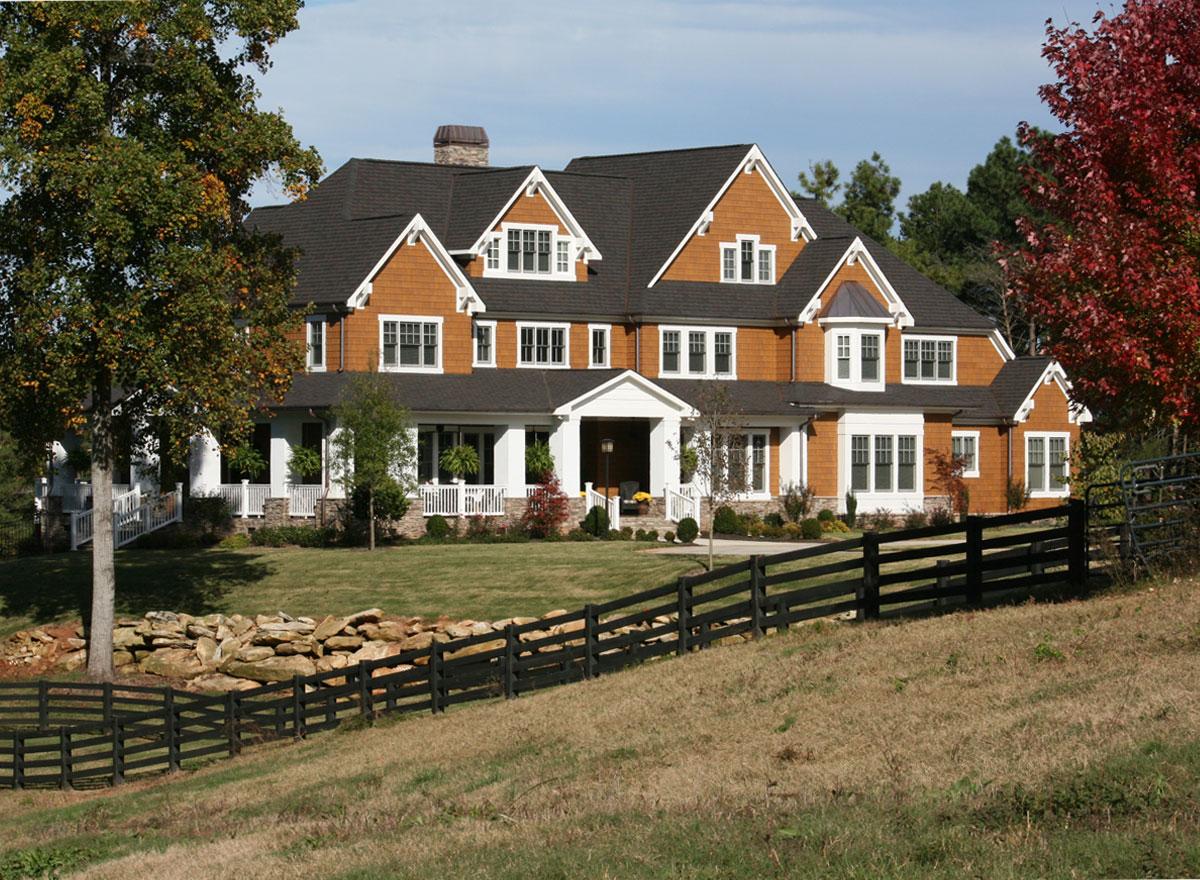 House plan exterior: Multi-story house with prominent gables, a wraparound porch, dormers, and a stone chimney.