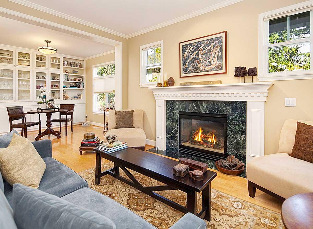 Living room with fireplace, built-in shelving, and natural light from windows. Seating includes a sectional sofa.