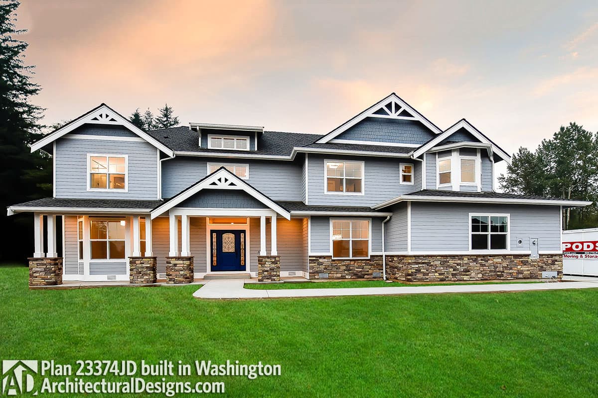 House plan exterior: two-story home with stone foundation, gabled dormers, prominent front porch with stone-clad columns.