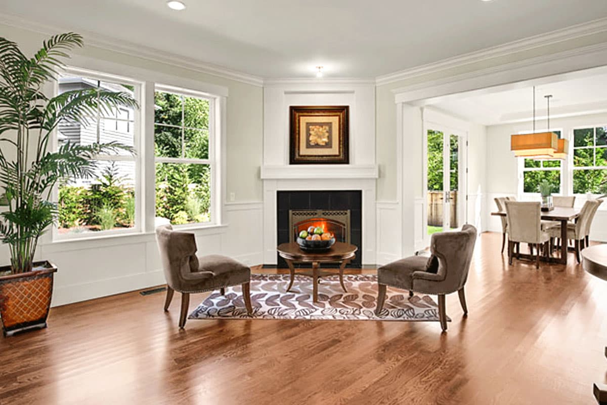 Living room interior with fireplace, large windows, and dining area beyond. Open layout with hardwood floors.