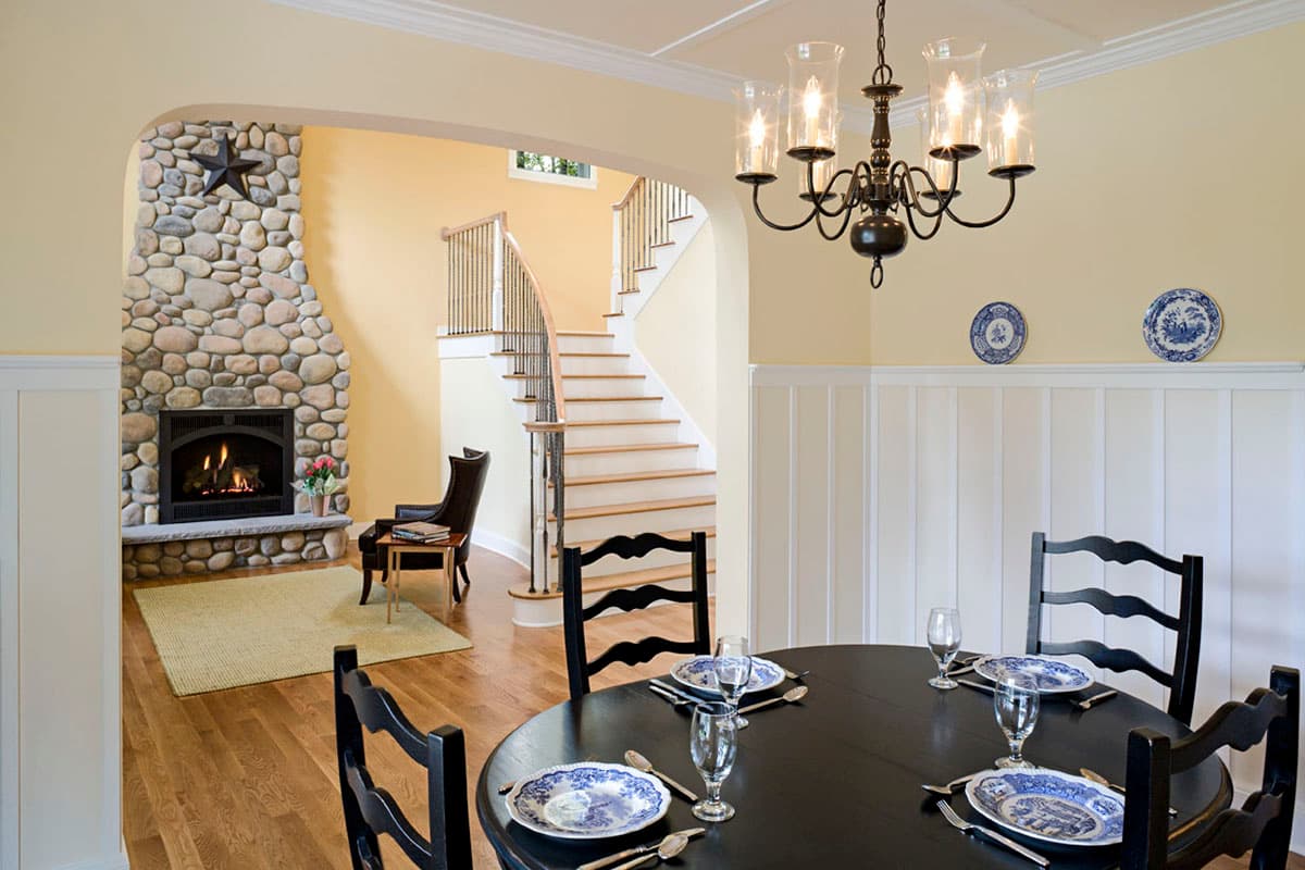 Interior view of dining room with black table and chairs, facing a curved staircase and stone fireplace.