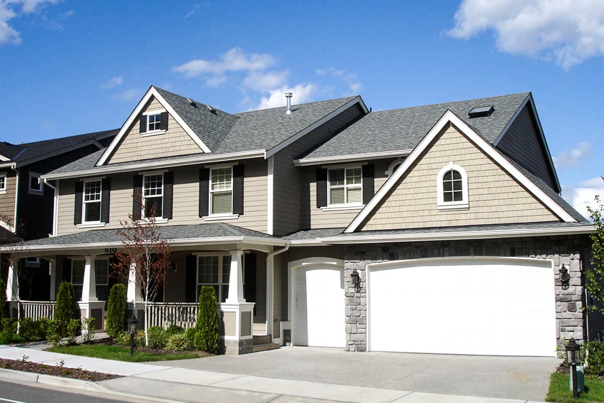 Two-story house plan exterior with wrap-around porch, dormers, and a side-facing two-car garage with stone accents.