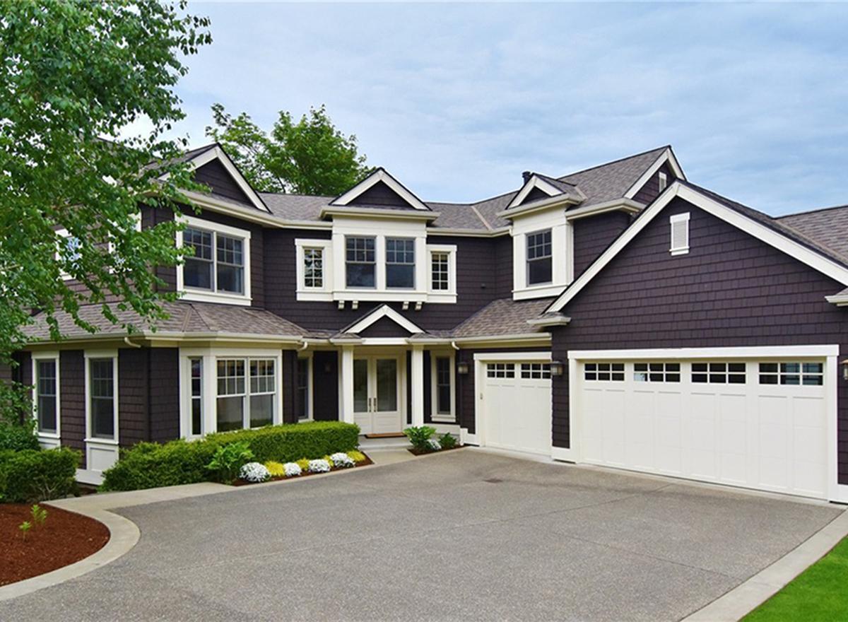 House plan exterior: Two-story home with dark shingle siding, multiple gables, dormers, and a three-car garage.