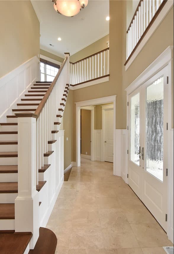 Interior view of a foyer with a wooden staircase, white wainscoting, and double doors with textured glass.