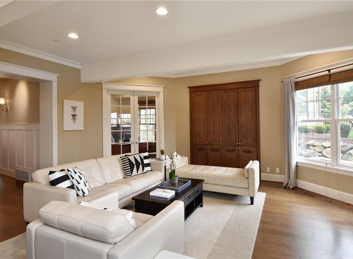Living room with white sectional sofa, coffee table, french doors, built-in wood cabinetry, and large windows.