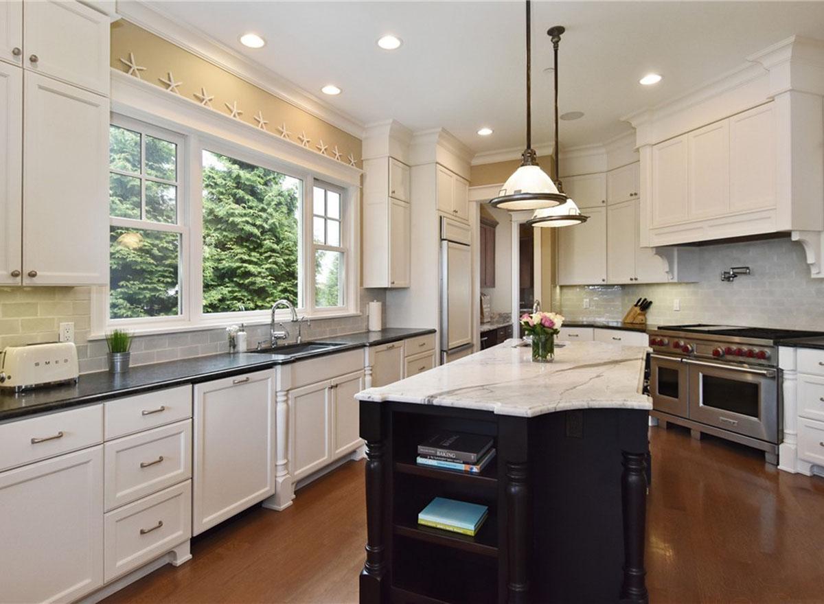 Kitchen with white cabinetry, large window, island with marble countertop, professional range, and pendant lighting.